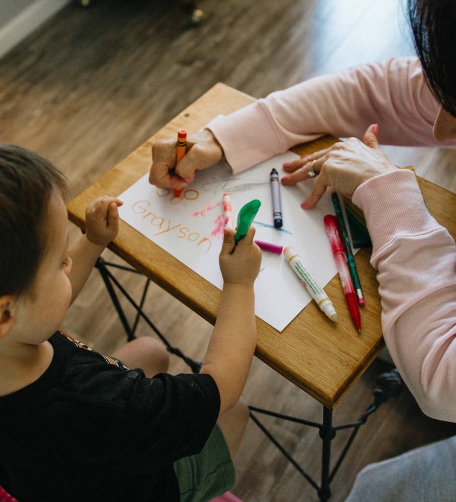 young-child-and-mentor-drawing-pictures-with-crayons-and-markers-on-small-desk